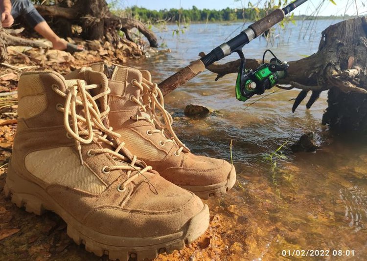 A pair of tactical boots and a fishing-rod near a lake