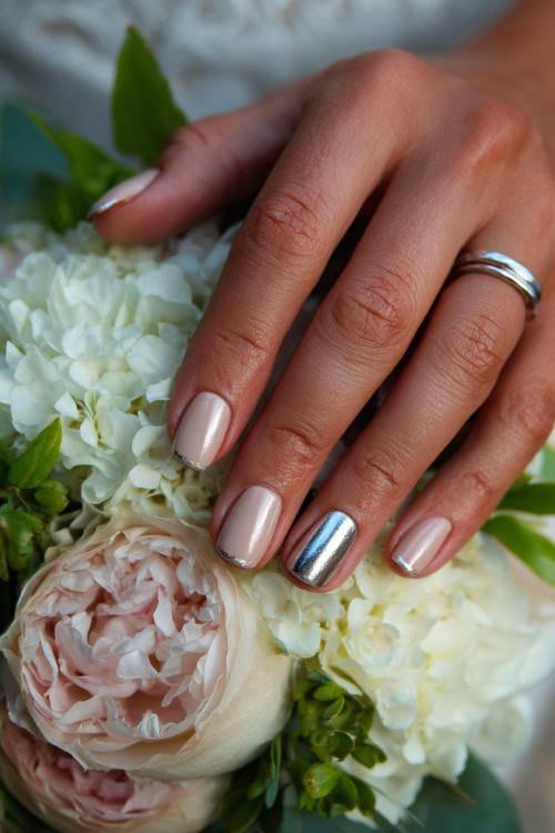 Bride’s fingers curled gently over bouquet, almond nails in pastel beige with chrome French tips and one accent nail in silver leaf foil 