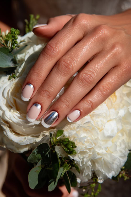 Bride’s fingers curled gently over bouquet, almond nails in pastel beige with chrome French tips and one accent nail in silver leaf foil 