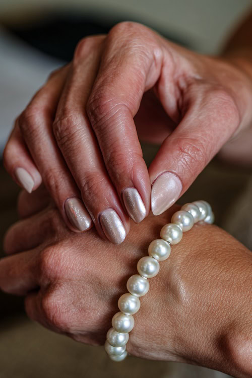 Bride’s hand adjusting pearl bracelet, short square nails in creamy ivory with chrome shimmer overlay and tiny crystal accents at the cuticle