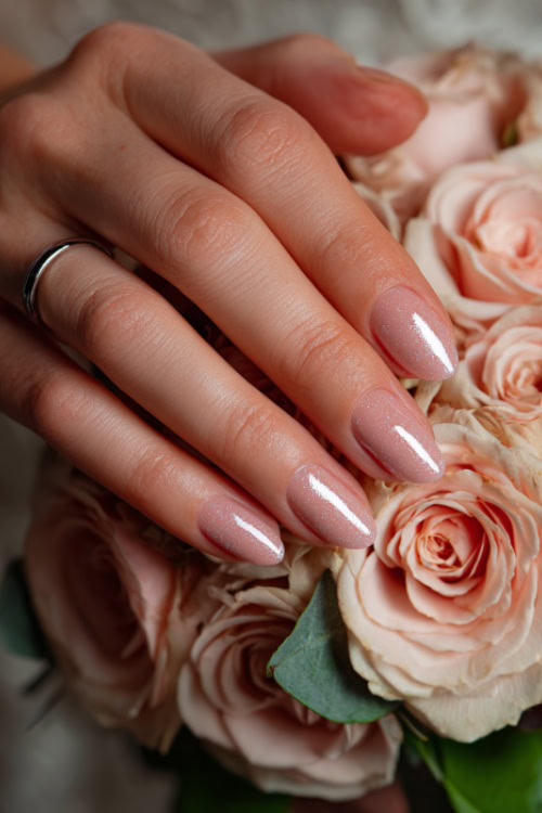 Bride’s hand gently holding a rose bouquet, medium almond nails in pastel pink with clear gloss and silver glitter gradient near the tips 