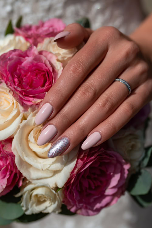 Bride’s hand gently holding a rose bouquet, medium almond nails in pastel pink with clear gloss and silver glitter gradient near the tips 