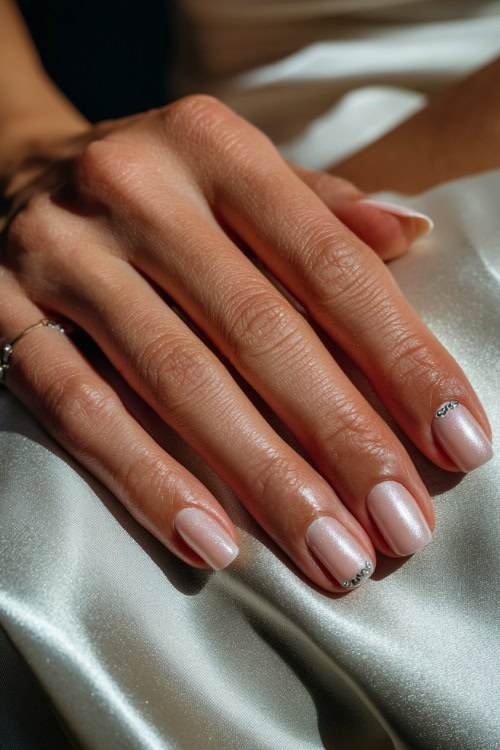 Bride’s hand gently resting on satin fabric, square nails in pale blush with soft shimmer overlay and crystal-studded cuticle accents