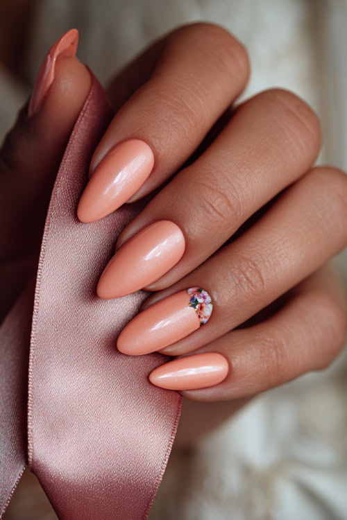 Bride’s hand holding a satin ribbon, almond-shaped nails in soft peach-pink with shimmer overlay and one floral accent on the ring finger 