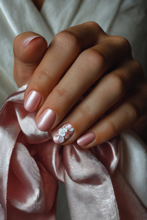 Bride’s hand holding a satin ribbon, almond-shaped nails in soft peach-pink with shimmer overlay and one floral accent on the ring finger 