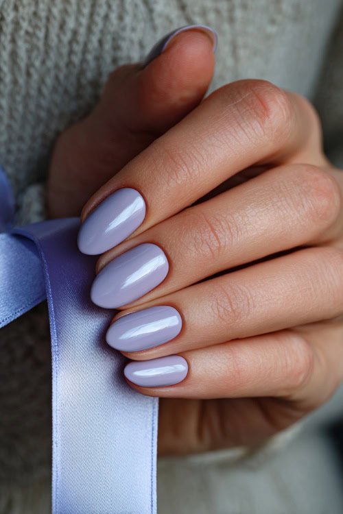Bride’s hand holding satin ribbon, short rounded nails in pale lavender with silver foil accents on the middle and ring fingers 