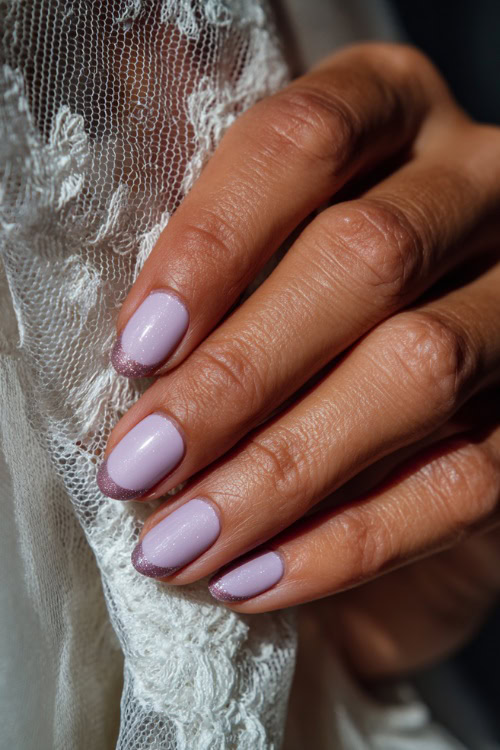 Bride’s hand holding veil edge, short oval nails in pastel lilac with glossy finish and subtle glitter gradient across the tips