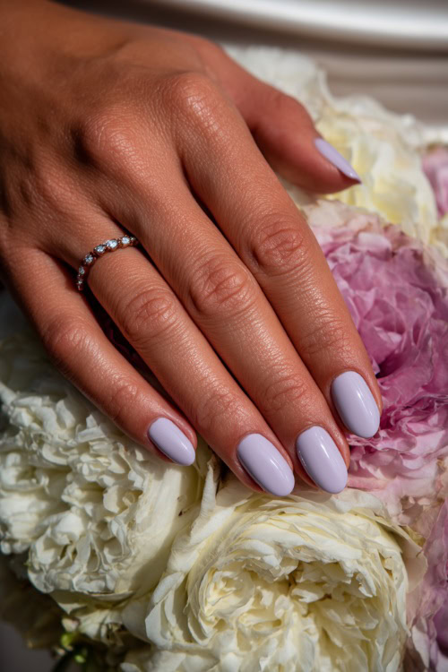 Bride’s hand resting beside wedding bouquet, medium almond nails in soft pastel lavender with a matte finish and white floral stamping 