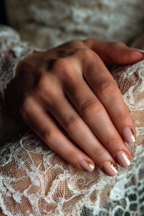 Bride’s hand resting on vintage lace fabric, square nails in soft rose-beige with satin finish and tiny gold foil flakes on the ring fingers 