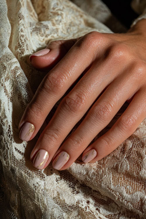 Bride’s hand resting on vintage lace fabric, square nails in soft rose-beige with satin finish and tiny gold foil flakes on the ring fingers