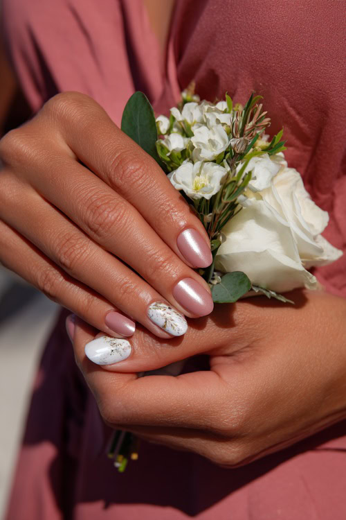 Bridesmaid’s hand placing a corsage, almond nails in soft pink with chrome shimmer and one accent nail in white floral stamping 