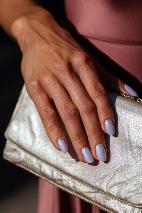 Bridesmaid’s hand resting beside a pearl clutch, medium almond nails in pastel lavender with chrome shimmer tips and tiny rhinestones near the cuticle