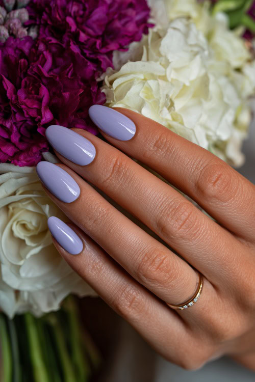 Bridesmaid’s hand resting beside bouquet stem, oval nails in pale lavender with subtle chrome sheen and floral pattern on one accent nail 