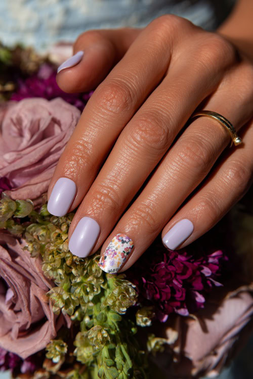 Bridesmaid’s hand resting beside bouquet stem, oval nails in pale lavender with subtle chrome sheen and floral pattern on one accent nail
