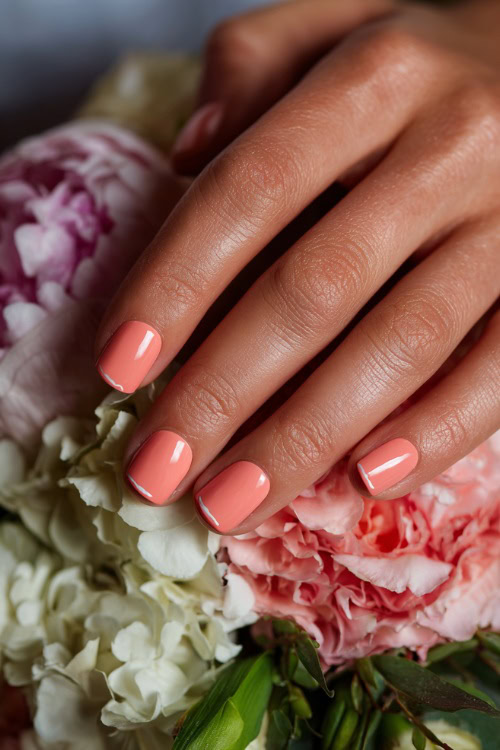 Bridesmaid’s hand resting beside floral decor, square nails in pastel coral with glossy finish and tiny white swirl details on the ring fingers 