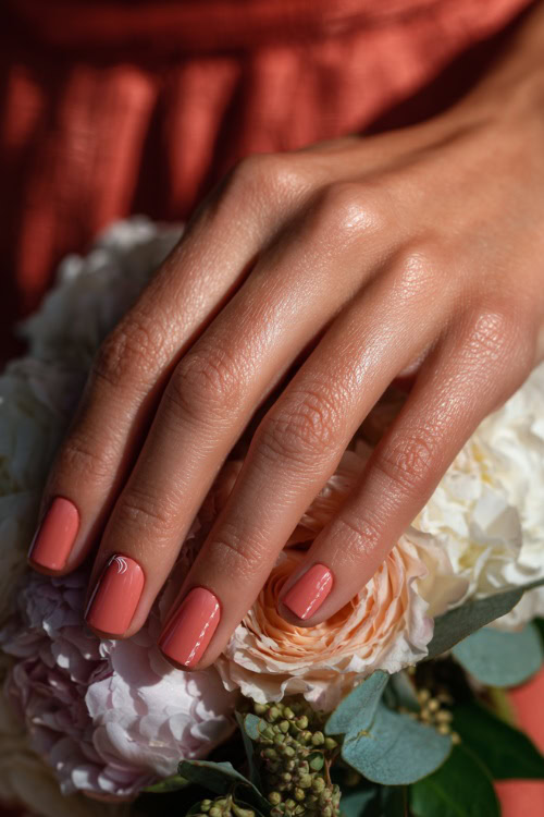 Bridesmaid’s hand resting beside floral decor, square nails in pastel coral with glossy finish and tiny white swirl details on the ring fingers