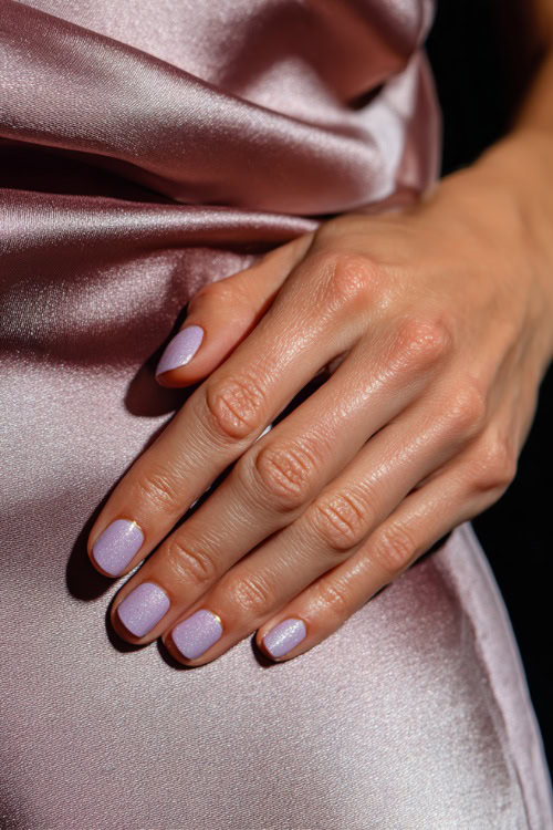 Bridesmaid’s hand resting on satin dress fabric, short square nails in pastel lavender with shimmer overlay and silver dot details at the base of each nail