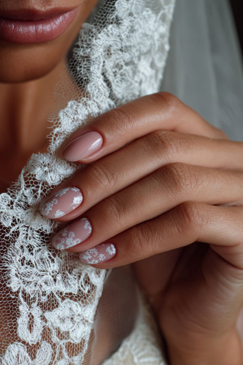 Close-up of bride’s hand gently holding a lace veil, almond-shaped nails in soft blush pink with glossy finish and delicate white floral decals 