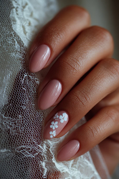 Close-up of bride’s hand gently holding a lace veil, almond-shaped nails in soft blush pink with glossy finish and delicate white floral decals 