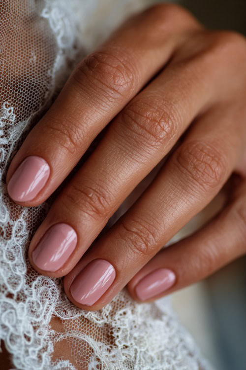 Close-up of bride’s hand resting on lace veil, almond-shaped nails in soft blush pink with classic French tips and glossy finish