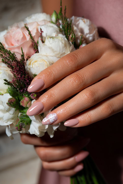 Close-up of bridesmaid’s hand holding a pastel bouquet, almond-shaped nails in soft blush pink with glossy finish and delicate white floral accents on two fingers 
