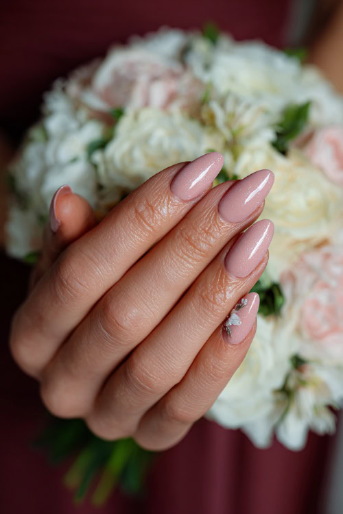 Close-up of bridesmaid’s hand holding a pastel bouquet, almond-shaped nails in soft blush pink with glossy finish and delicate white floral accents on two fingers