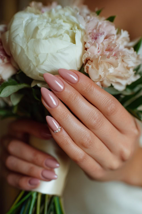 Close-up of bridesmaid’s hand holding a silk bouquet ribbon, almond-shaped nails in soft blush pink with glossy finish and delicate pearl accents along the cuticle 