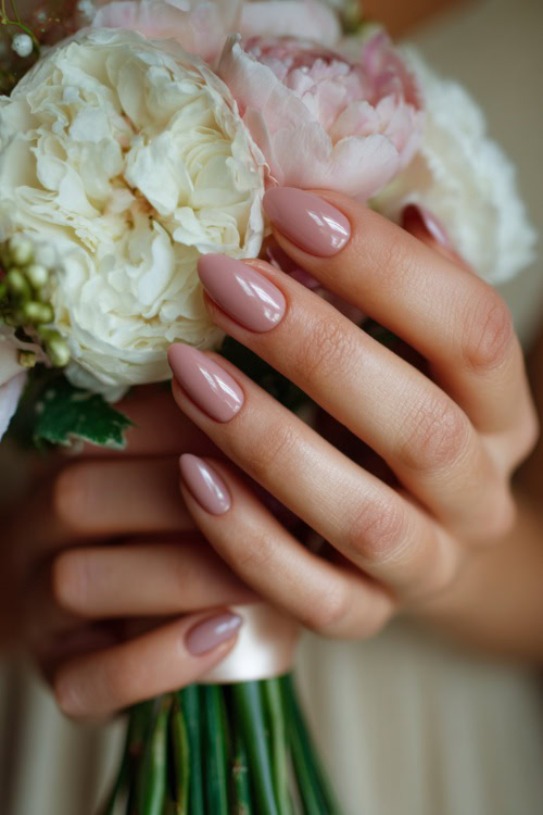 Close-up of bridesmaid’s hand holding a silk bouquet ribbon, almond-shaped nails in soft blush pink with glossy finish and delicate pearl accents along the cuticle 