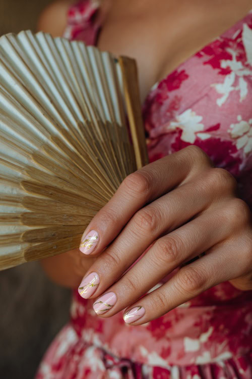 Close-up of bridesmaid’s hand holding a silk fan, short oval nails in soft pink with matte finish and one accent nail featuring delicate gold line art 