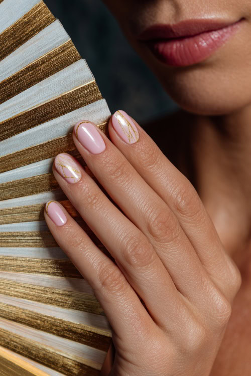 Close-up of bridesmaid’s hand holding a silk fan, short oval nails in soft pink with matte finish and one accent nail featuring delicate gold line art 