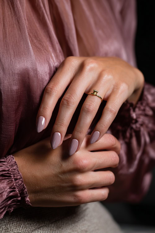 Close-up of fingers brushing chiffon gown, short almond nails in pastel mauve with clear gloss and a single gold charm on the ring finger 