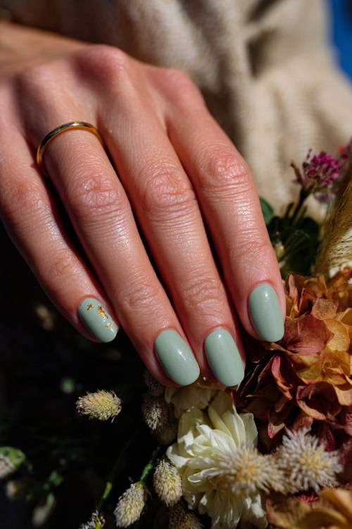 Close-up of guest’s hand beside wedding centerpiece, short rounded nails in pastel green with glossy topcoat and tiny gold flake details on two fingers 