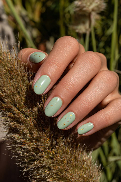 Close-up of guest’s hand beside wedding centerpiece, short rounded nails in pastel green with glossy topcoat and tiny gold flake details on two fingers