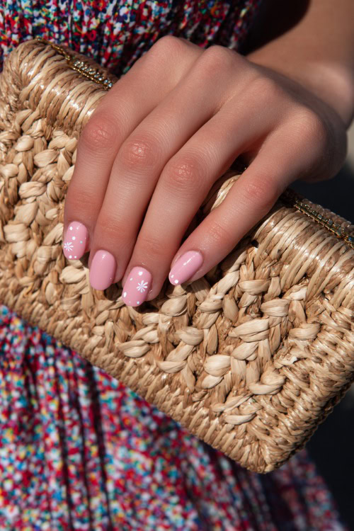 Close-up of guest’s hand holding a woven clutch, short almond nails in pastel pink with glossy finish and tiny white floral decals on two fingers