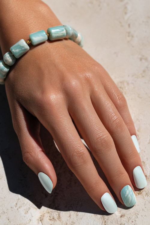 Close-up of hand adjusting bracelet, short square nails in pastel mint with marble effect and soft shimmer overlay