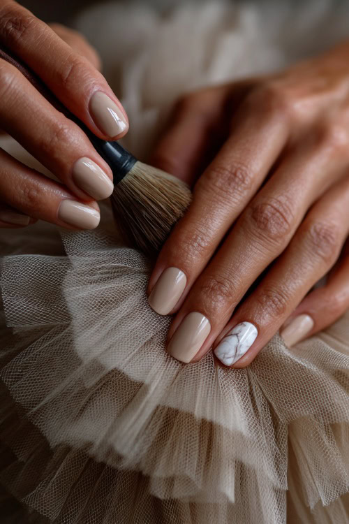 Close-up of hand brushing tulle gown, square nails in creamy beige with marble effect on one accent nail and glossy finish 