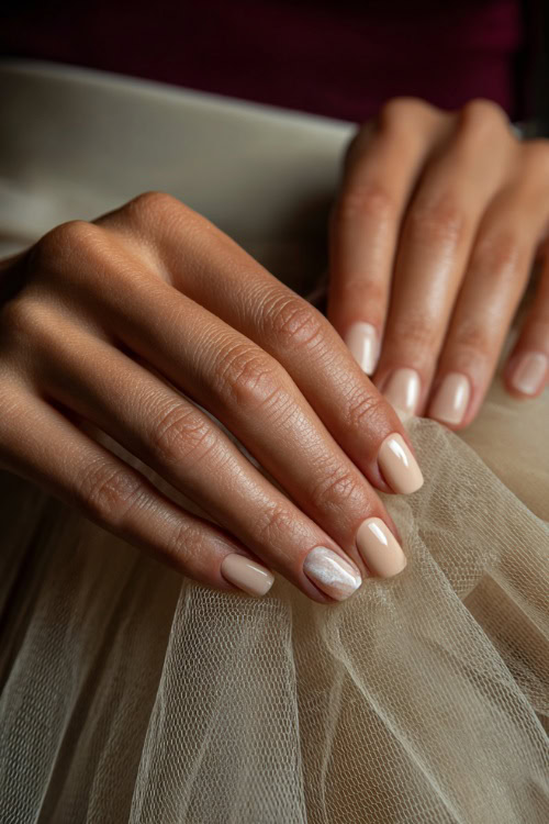 Close-up of hand brushing tulle gown, square nails in creamy beige with marble effect on one accent nail and glossy finish 