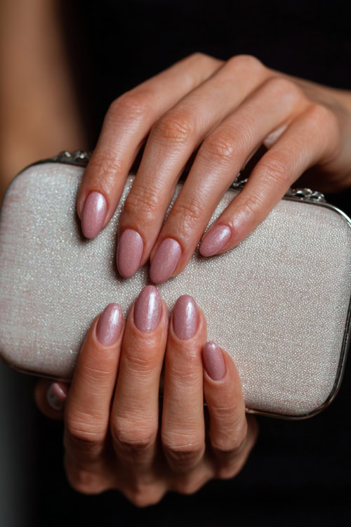 Close-up of hand holding a bridal clutch, short almond nails in pale pink with chrome shimmer overlay and subtle crystal accents 