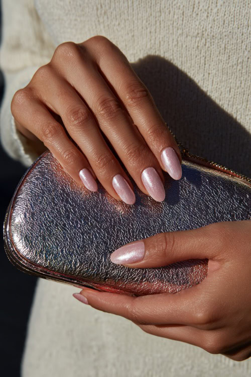 Close-up of hand holding a bridal clutch, short almond nails in pale pink with chrome shimmer overlay and subtle crystal accents 