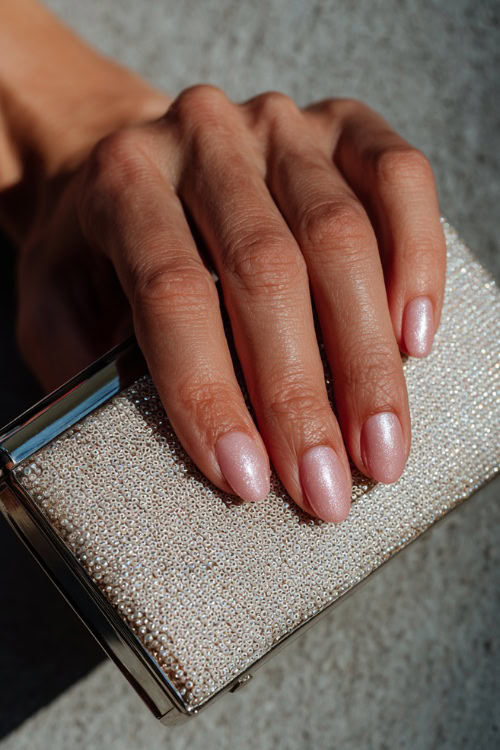 Close-up of hand holding a pearl clutch, short square nails in soft blush pink with glossy finish and subtle silver glitter on two fingers 