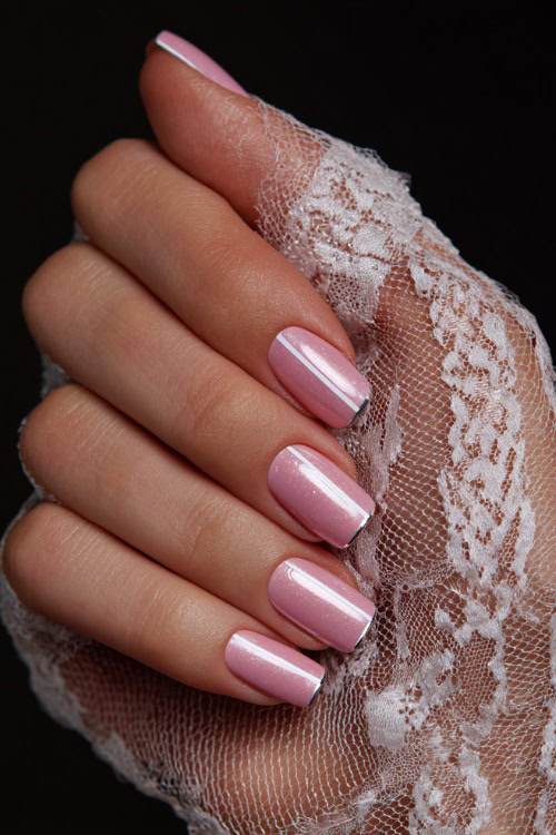 Close-up of hand holding lace glove, short square nails in light pink with glossy topcoat and a thin silver line across the center of each nail 