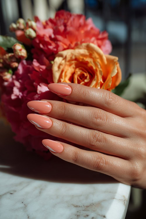 Close-up of hand placing a bouquet on the table, soft peach nails in ballerina shape with glossy finish and subtle white swirl design (2)