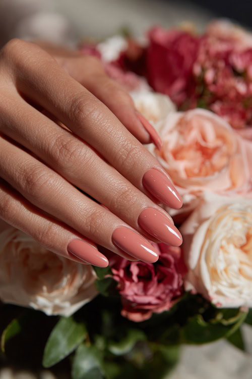 Close-up of hand placing a bouquet on the table, soft peach nails in ballerina shape with glossy finish and subtle white swirl design