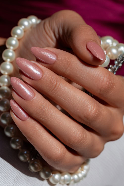 Close-up of hand placing pearl hair accessory, almond nails in champagne pink with chrome shimmer and subtle crystal cuticle accents