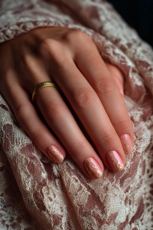 Close-up of hand resting on vintage lace fabric, square-shaped nails in pale peach with satin finish and delicate gold foil details 