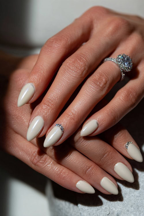 Elegant bridal hand adjusting earrings, ballerina-shaped nails in creamy white with chrome finish and tiny crystal accents at the cuticle