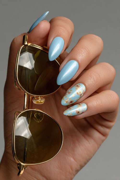 Elegant guest’s hand holding sunglasses, short almond nails in pastel blue with chrome finish and minimalist floral pattern on two fingers 