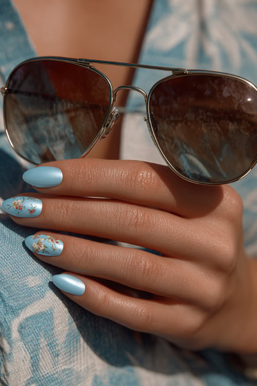 Elegant guest’s hand holding sunglasses, short almond nails in pastel blue with chrome finish and minimalist floral pattern on two fingers