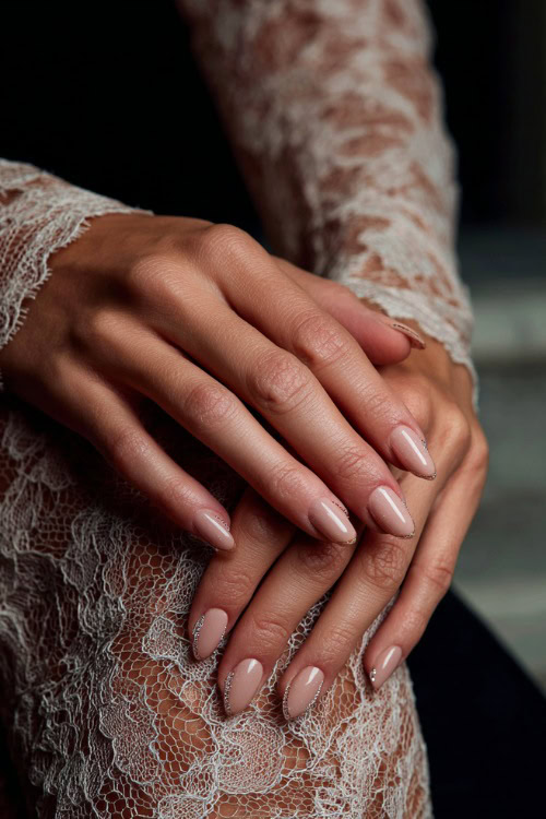 Elegant hand adjusting lace dress sleeve, almond nails in soft beige with glossy finish and tiny crystal-studded cuticle details on each finger
