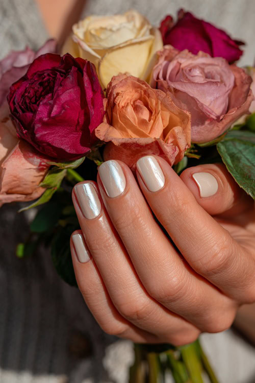 Elegant hand holding a pastel rose bouquet, square nails in sheer ivory with glossy finish and delicate silver leaf foil on two fingers